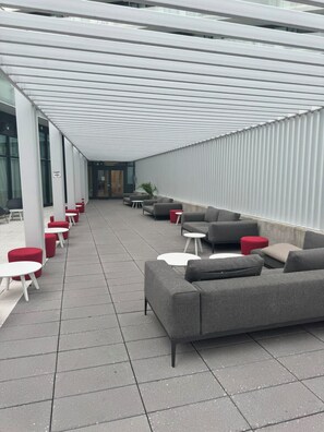 An outdoor seating area with grey sofas and red ottomans, a covered walkway, and a building entrance. - The Modern Retreat | Luxury 2 Bed, 2 Bath Condominium (Mississauga)