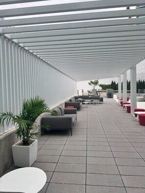 A covered outdoor seating area with sofas and tables, a potted plant, and a view of the surrounding area. - The Modern Retreat | Luxury 2 Bed, 2 Bath Condominium (Mississauga)