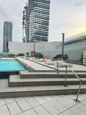 A rooftop pool area with a view of modern buildings, a metal railing, and a sign with text. - The Modern Retreat | Luxury 2 Bed, 2 Bath Condominium (Mississauga)