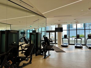 Un gimnàs modern amb diversos equips d'exercici, grans finestres i vistes a la ciutat.