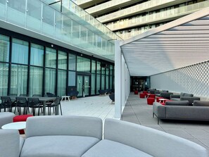 Zona exterior amb mobiliari modern, façana de vidre d'un edifici i passatge cobert.