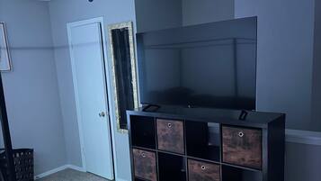A room with a ceiling fan, a large flat-screen TV, a dark wooden storage unit, a door, and a framed mirror.