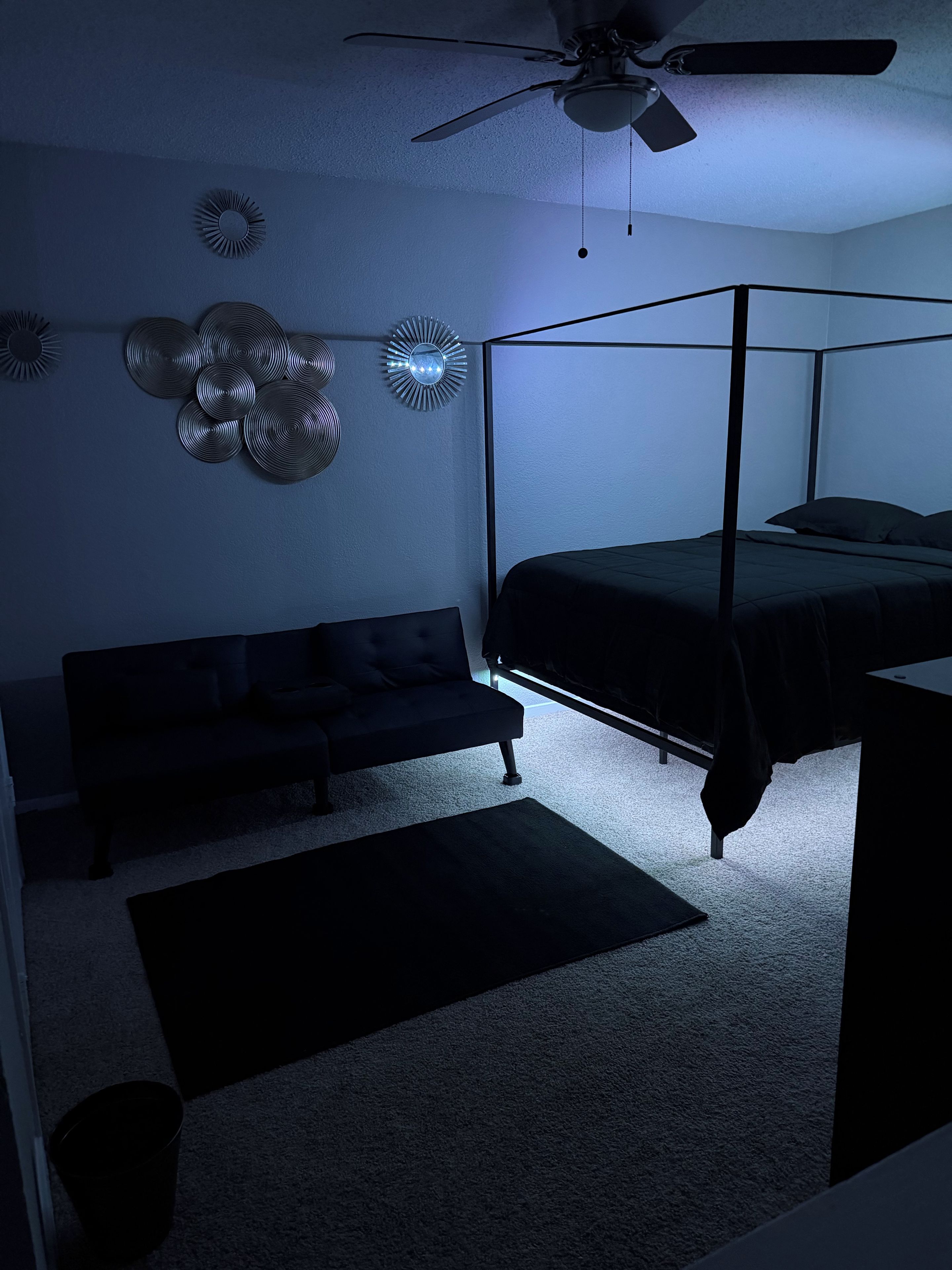 A bedroom with a four-poster bed, a sofa, and decorative wall sconces.