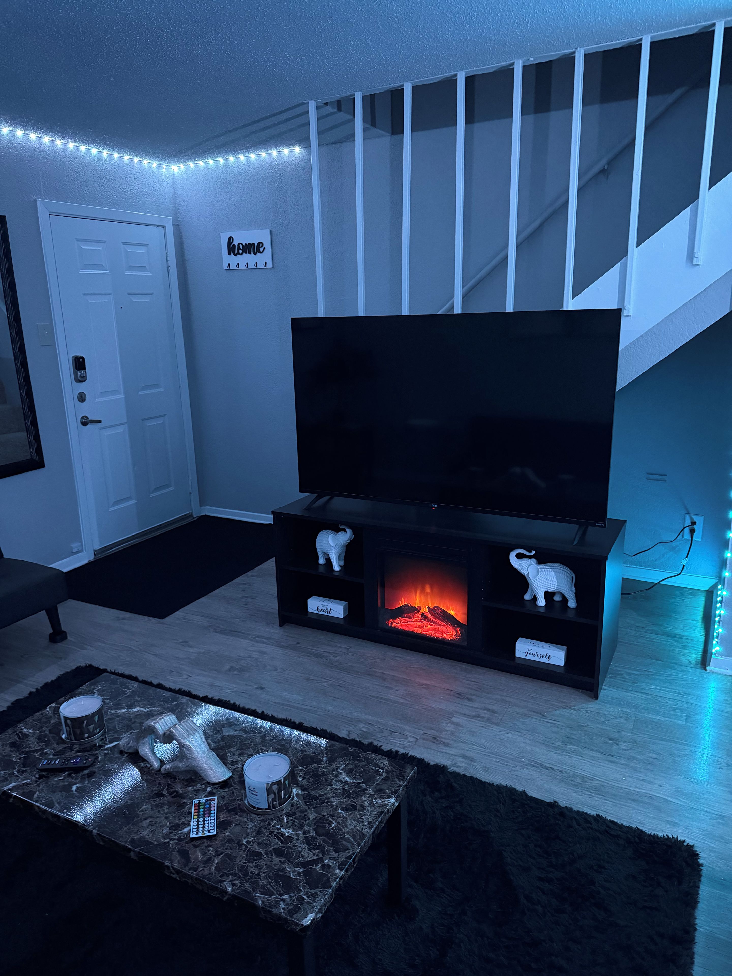 A living room with a flat-screen TV, a fireplace, and a staircase.