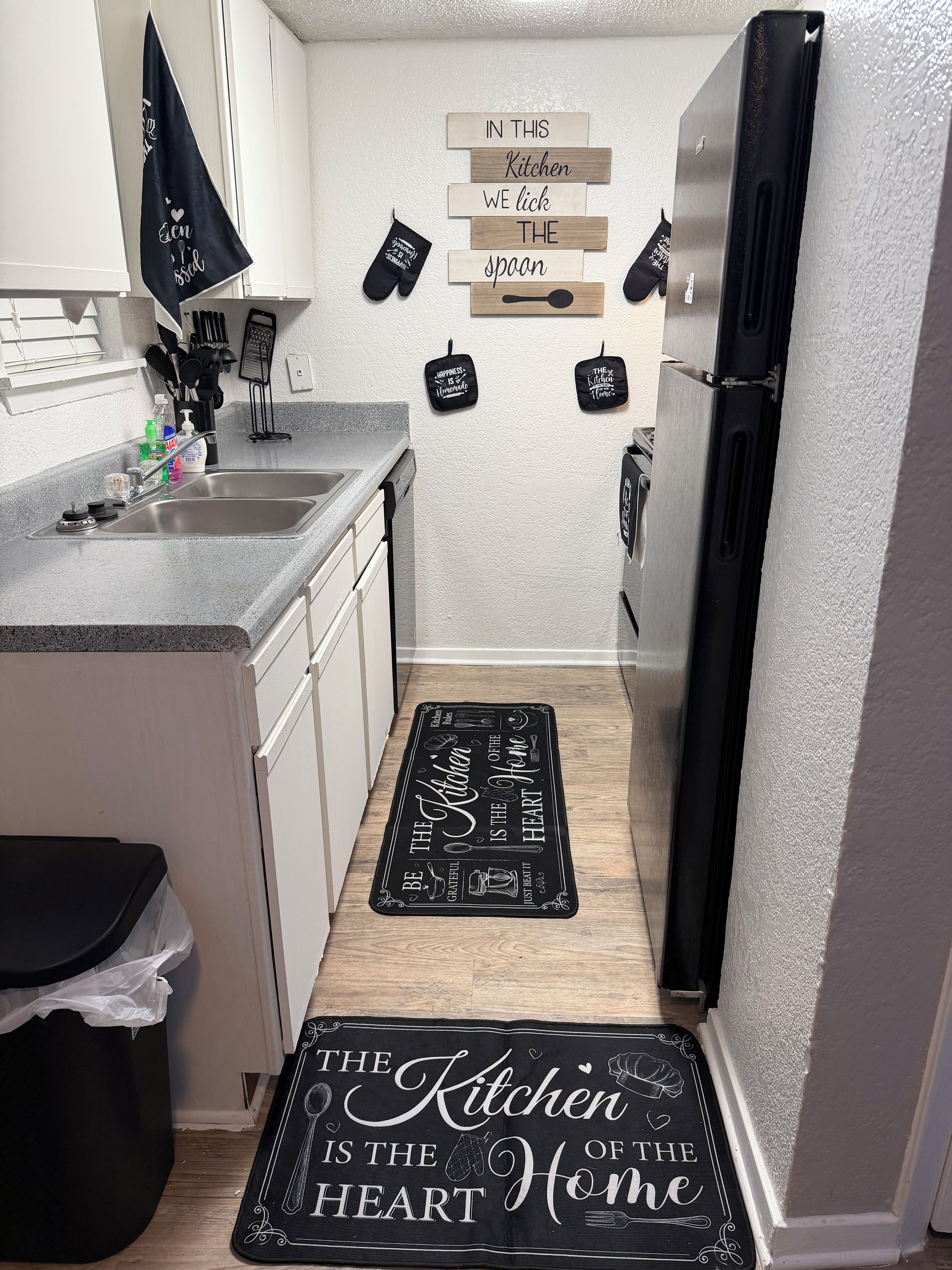 A kitchen with a black and white backsplash, a stainless steel refrigerator, and a wooden floor.