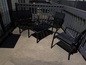 A balcony with a black metal table and chairs, a black doormat, and a metal railing. -  A cozy stylish 2- story loft with a peaceful vibe (Addison)