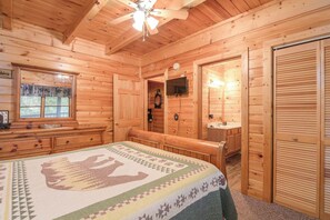 A wooden cabin interior with a bed, a dresser, a television, and a bathroom. - Two King Bedrooms | Hot Tub | Couples’ Escape (Sevierville)