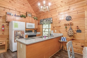 A wooden cabin kitchen with a refrigerator, stove, microwave, and a chandelier. - Two King Bedrooms | Hot Tub | Couples’ Escape (Sevierville)