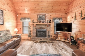 A log cabin interior with a fireplace, leather sofa, television, and decorative items. - Two King Bedrooms | Hot Tub | Couples’ Escape (Sevierville)