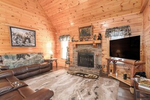 Ein Holzblockhaus-Interieur mit Ledersofa, Kamin, Fernseher und einem Teppich mit Bärenmotiv.