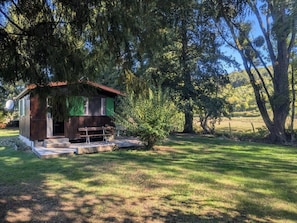 A small wooden cabin with a bench outside, surrounded by trees and grass. - The Echo of the Rut - BOUZANCOURT (BOUZANCOURT)