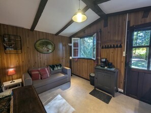 A cozy room with wooden walls, a sofa with cushions, a coffee maker, and a window with a view of greenery. - The Echo of the Rut - BOUZANCOURT (BOUZANCOURT)