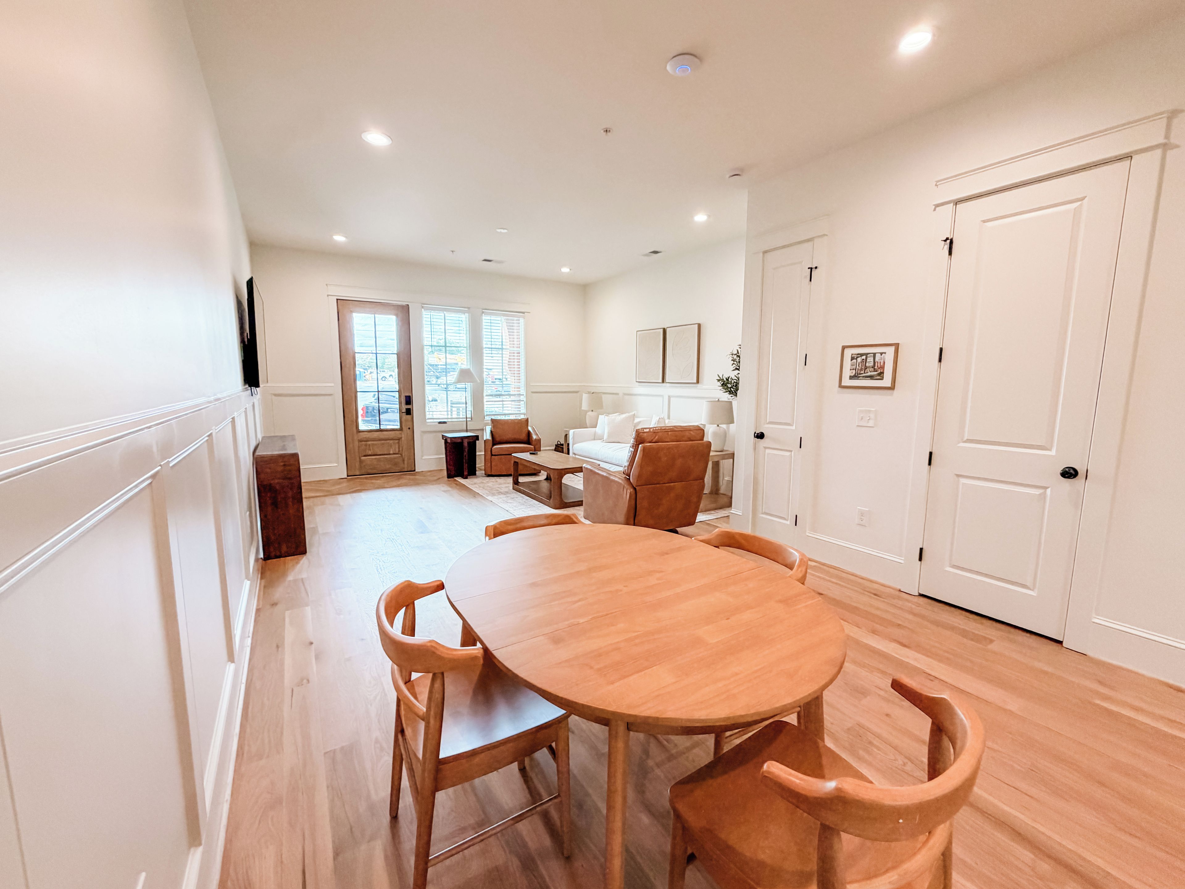Un grand espace à manger avec une table et des chaises en bois, une cuisine à l’arrière-plan et une porte donnant sur une autre pièce.