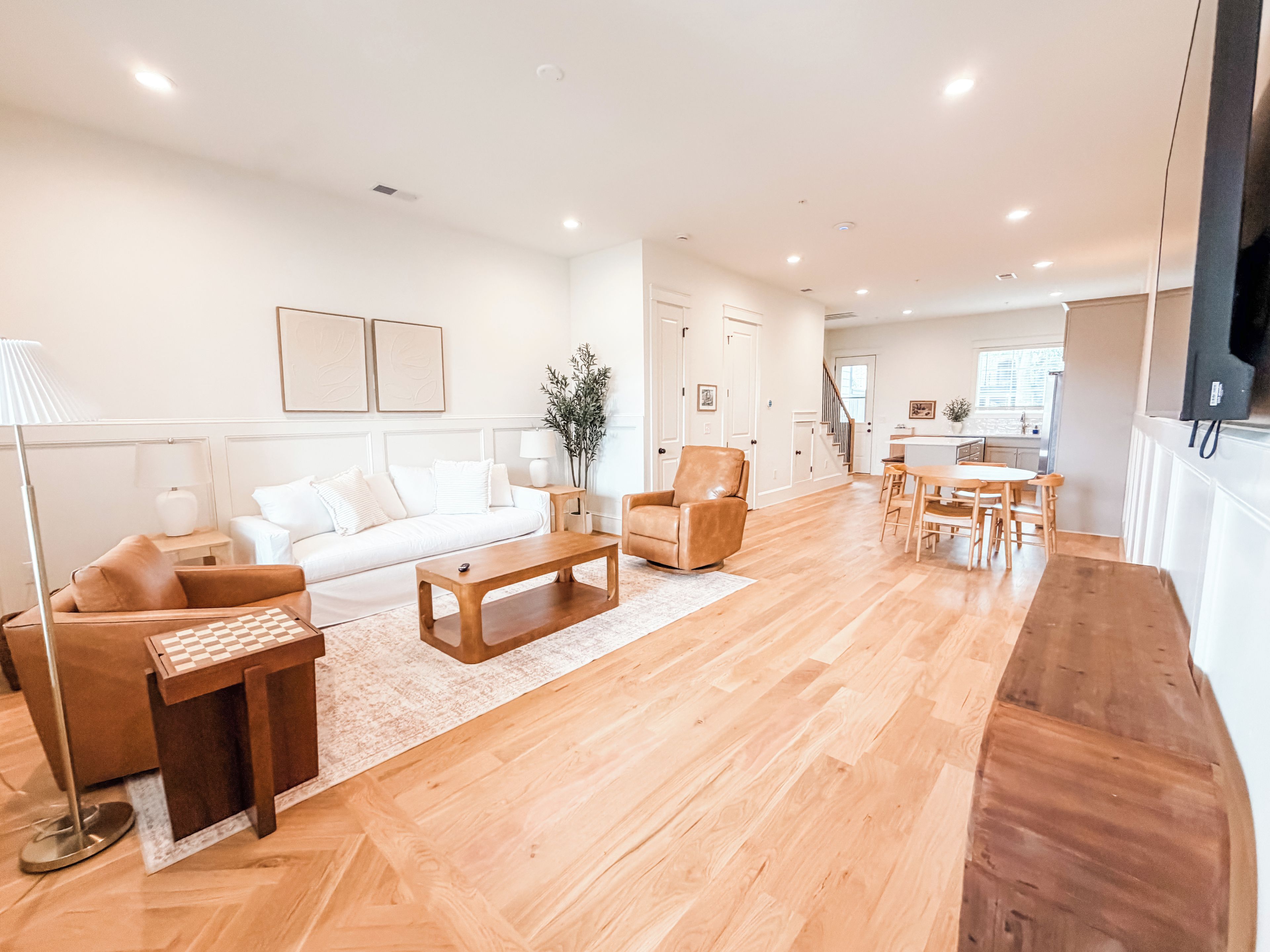Un salon moderne comprenant un canapé, une table basse et des fauteuils, un coin cuisine avec une table à manger, et un escalier menant à un niveau supérieur.