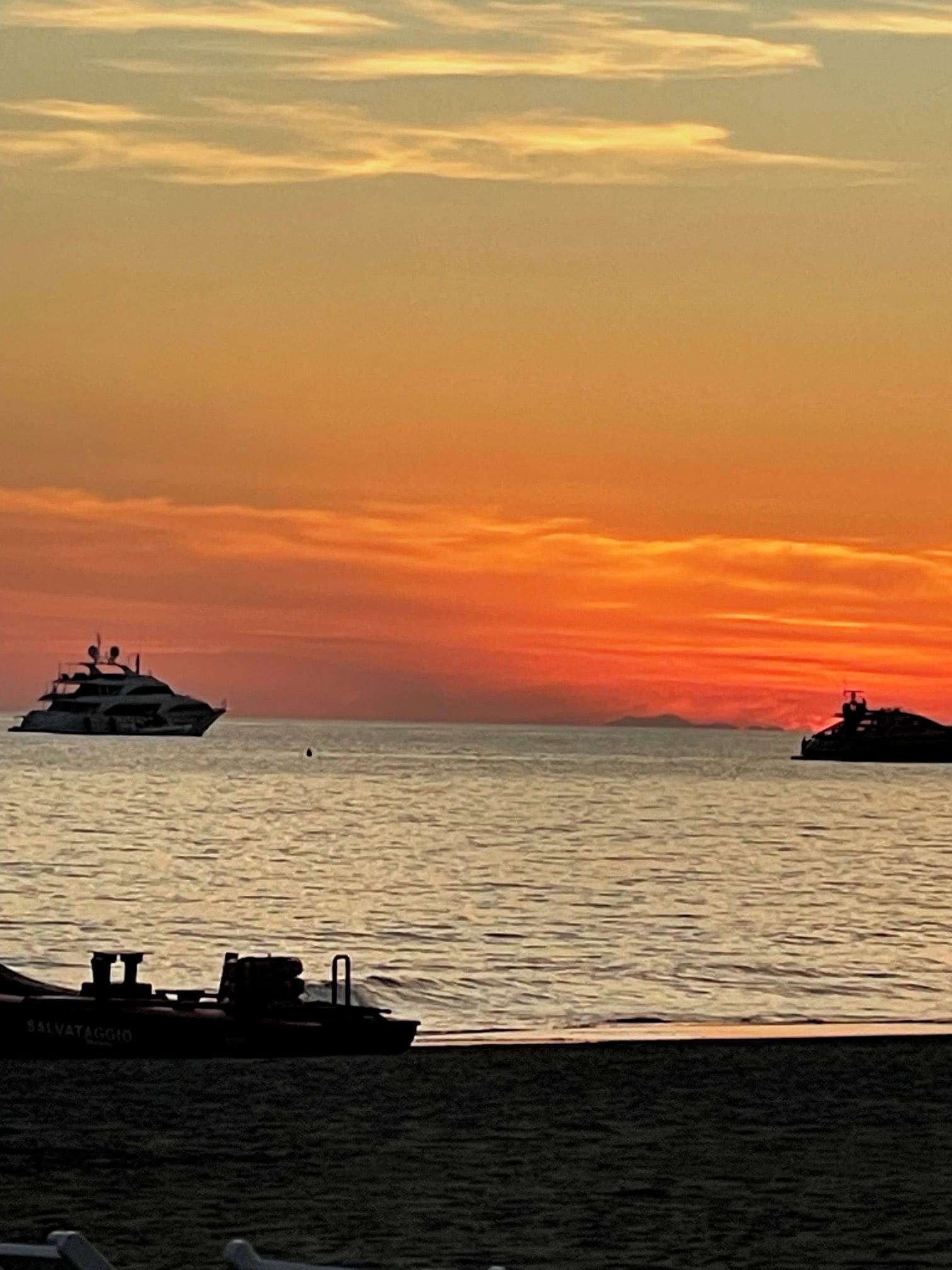 A sunset over the ocean with two boats.