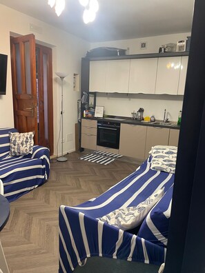 A compact living space with a kitchenette, two striped beds, a wooden door, and a small dining area. - A 13-minute bike ride from downtown Forte dei Marmi: apartment with a terrace (Ripa- Pozzi-Ponterosso)