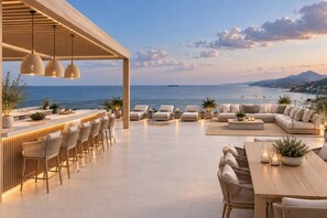 Ein Außenbereich mit Sitzgelegenheiten, einer Bar, Lounge-Stühlen und Sofas mit Blick auf die Küste.