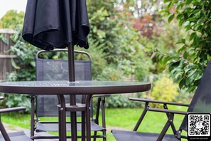 Een ronde tafel met een net bovenkant, omringd door twee stoelen met armleuningen, een zwarte parasol en een QR-code voor korting.