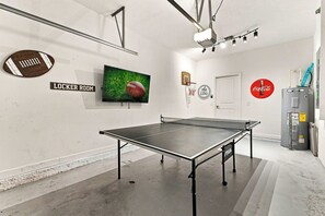 Ein Zimmer mit Tischtennisplatte, Fernseher, Coca-Cola-Schild und Warmwasserbereiter.