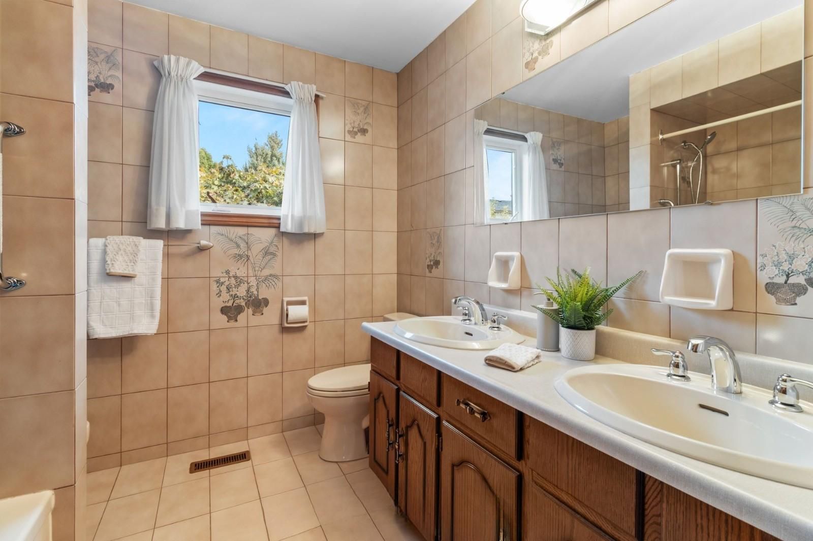 A bathroom with two sinks, a toilet, a shower, and a window with curtains.
