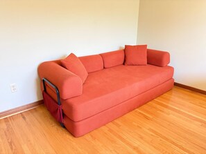 Een rode bank met een metalen frame en een rood kussen, tegen een witte muur, met een houten vloer.