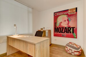 A minimalist office space with a wooden desk, a single chair, a desk lamp, and a poster on the wall. - w* | Amazing 2BR in Zona T (Bogotá)