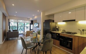A modern kitchen with a dining area, featuring a glass table, chairs, a refrigerator, stove, and a coffee maker. - w* | Deluxe 2BR w/ Terrace in Miraflores (Miraflores)