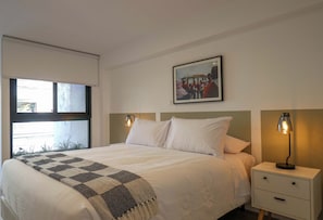 A hotel room with a bed, bedside tables, a lamp, a window, and a framed picture on the wall. - w* | Deluxe 2BR w/ Terrace in Miraflores (Miraflores)