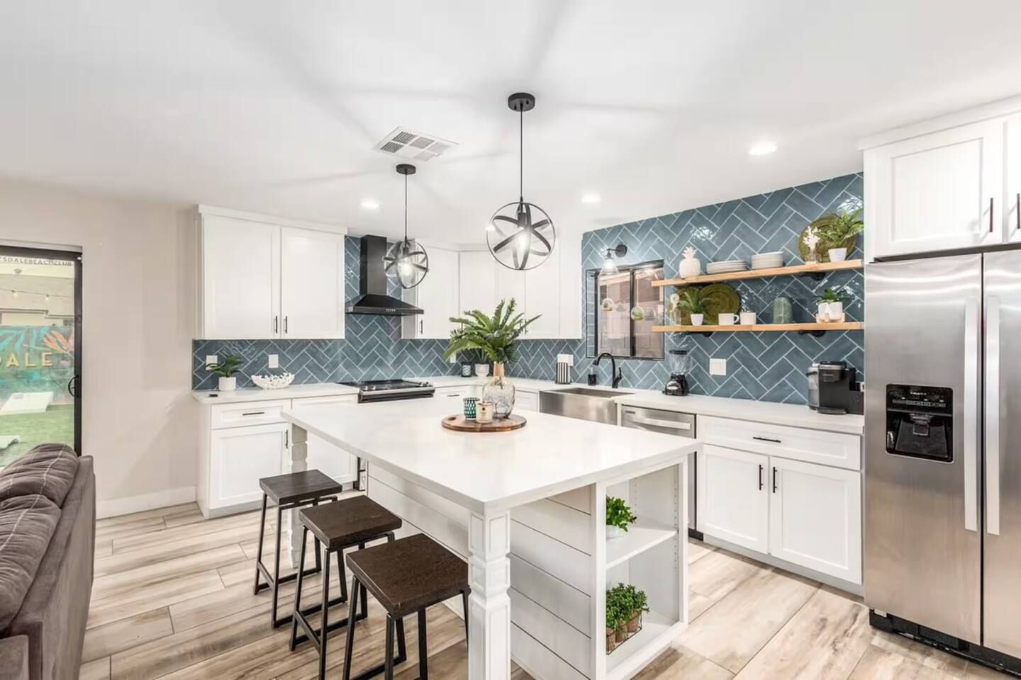 A modern kitchen with white cabinetry, a central island with stools, a stainless steel refrigerator, and a herringbone-patterned backsplash.