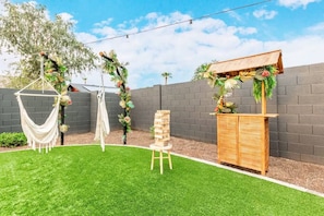 Ein Garten mit einer Hängematte, einer Holzbank und einem Zierpflanzgefäß.