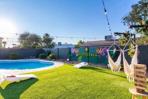 Ein Garten mit Swimmingpool, einer Hängematte und einem Wandgemälde.