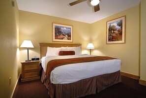 Quarto de hotel com uma cama, duas luminárias de cabeceira, mesa de cabeceira e duas quadros na parede.