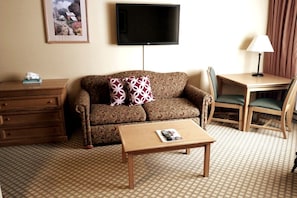 A hotel room with a sofa, a small table, a TV mounted on the wall, a lamp, and a picture frame. - 379 Slopeside Studio King Bed Kitchen @Mt.CB (Crested Butte)
