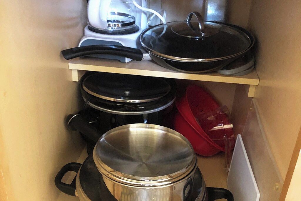 A kitchen with a stove, pots, and a red pot on a shelf.