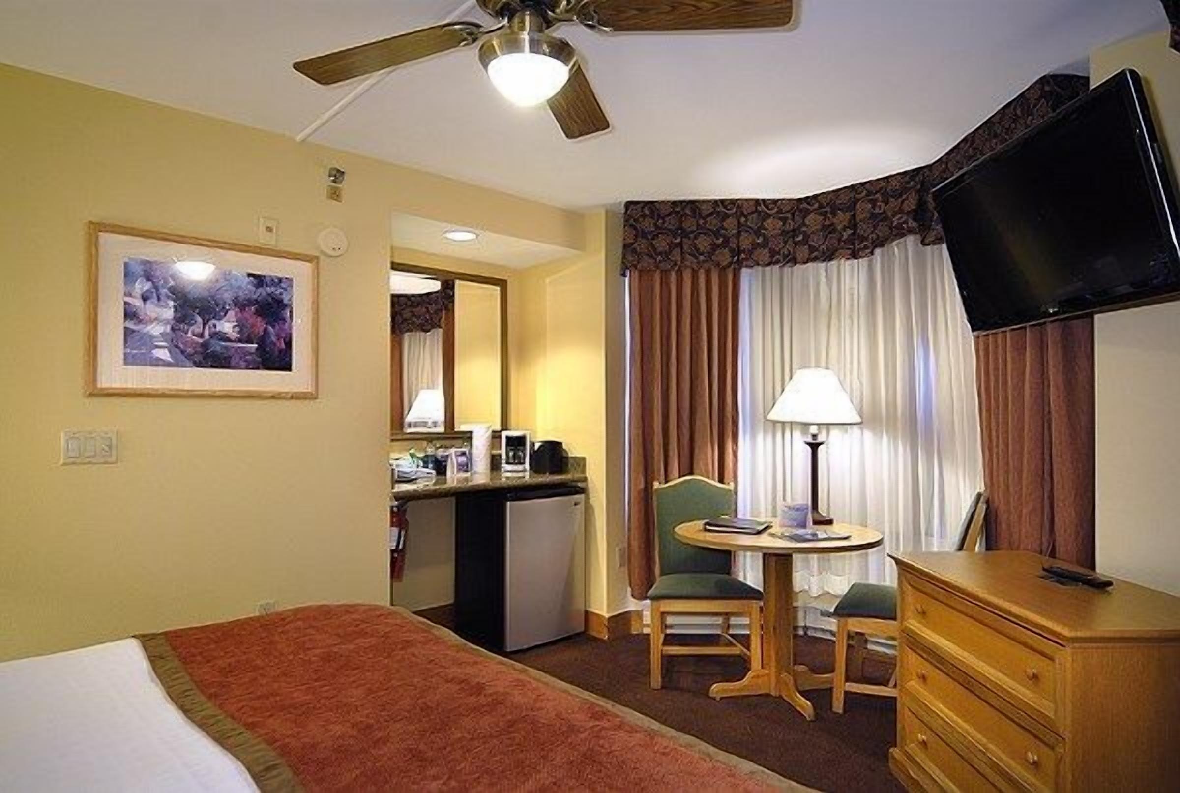 A hotel room with a bed, a desk, a chair, a television, and a small kitchenette.