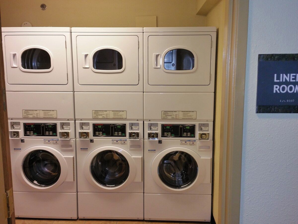 Une rangée de trois machines à laver à chargement frontal, empilées les unes sur les autres, dans une buanderie.