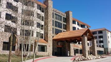 Un hotel de varios pisos con fachada de piedra, un acceso cubierto y un cielo azul despejado.