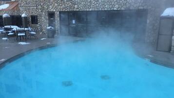 Edificio de piedra con piscina que emite vapor, rodeado de mobiliario de exterior.