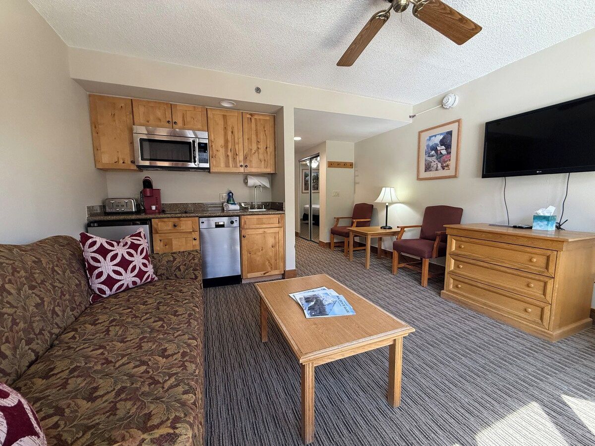 A compact living space with a kitchenette, a sofa, a coffee table, a TV, and a dining area.