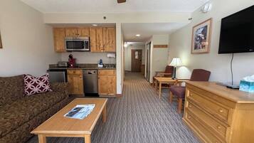 A compact living space with a kitchenette, a sofa, a coffee table, a TV, and a desk with drawers.