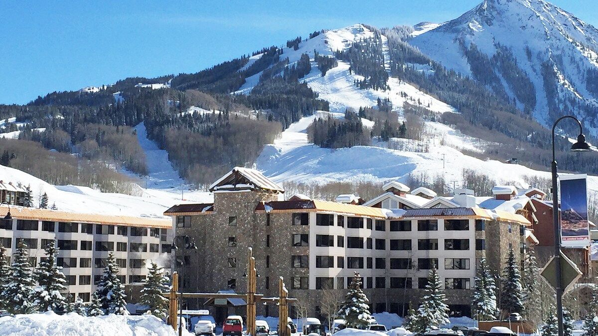 A hotel with multiple floors, a ski slope in the background, and snow-covered surroundings.