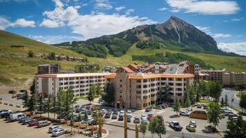 A multi-story hotel with a parking lot, surrounded by greenery and a mountain in the background.