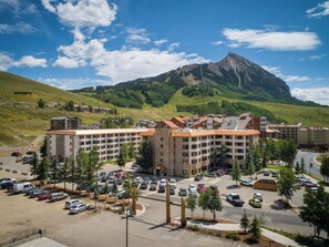 A multi-story hotel with a parking lot, surrounded by greenery and a mountain in the background. - NEW LISTING - 515 slope side 2 king view of Mt. Crested Butte (Crested Butte)