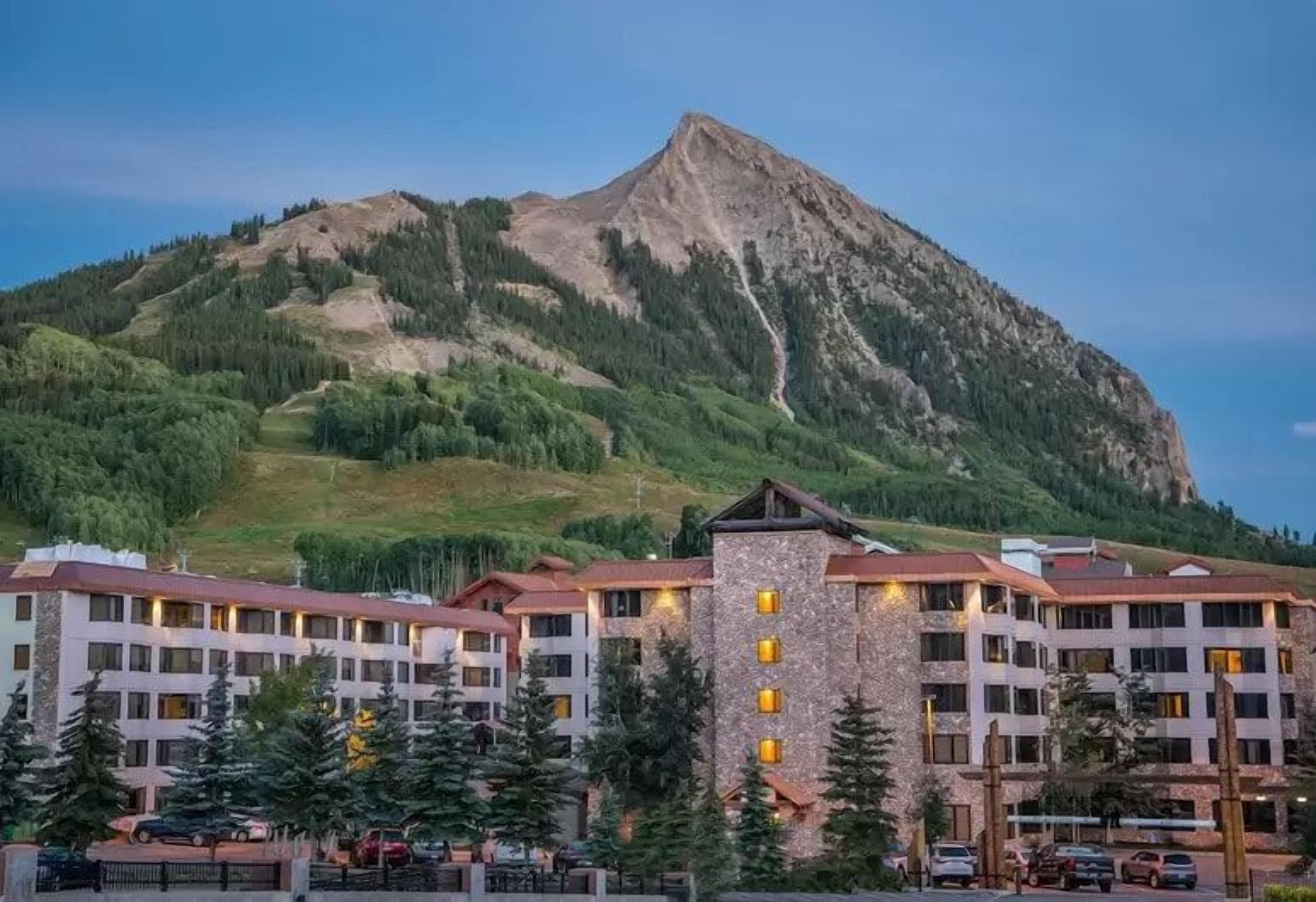 A hotel with multiple floors, a central tower, and a mountain backdrop.