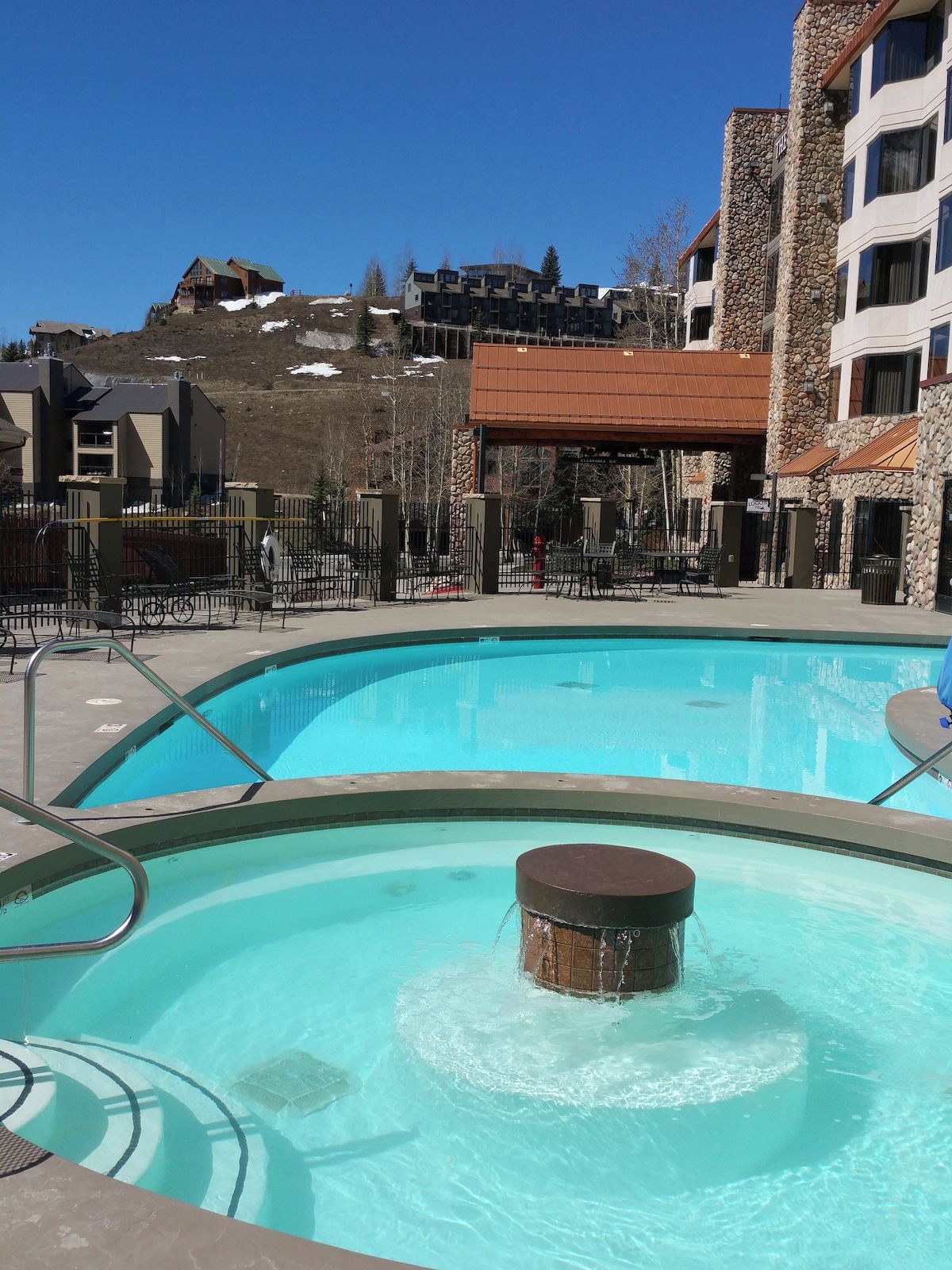 A swimming pool with a hot tub in the center, surrounded by a fenced area with lounge chairs.