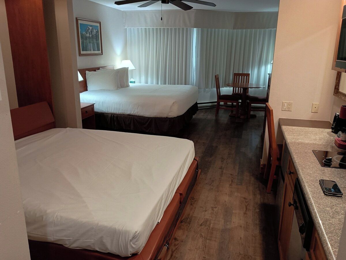 A hotel room with two beds, a dining area, and a kitchenette.