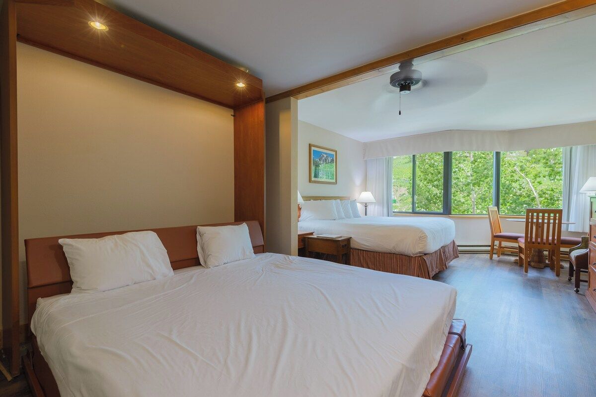 A hotel room with two beds, a desk, and a chair.