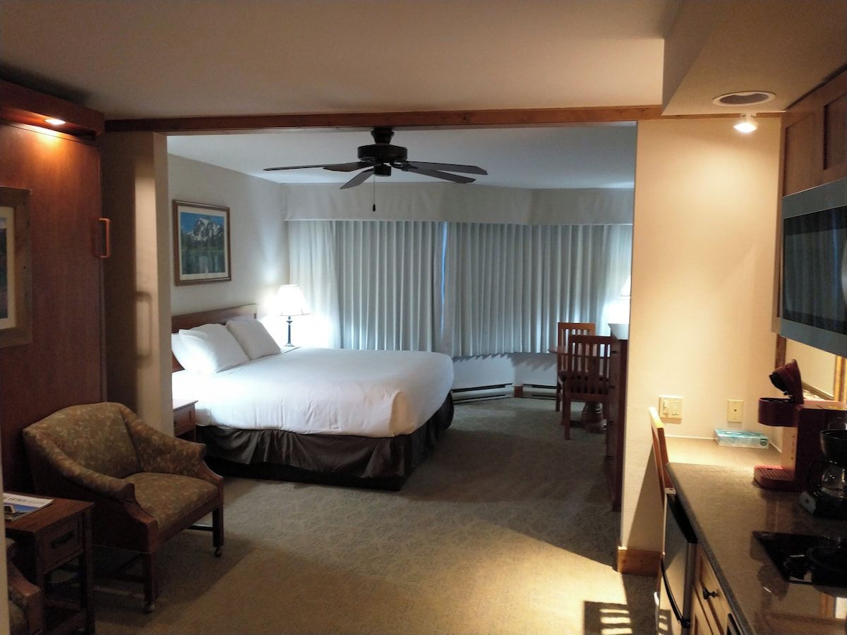 A hotel room with a bed, a chair, a desk, a television, and a ceiling fan.
