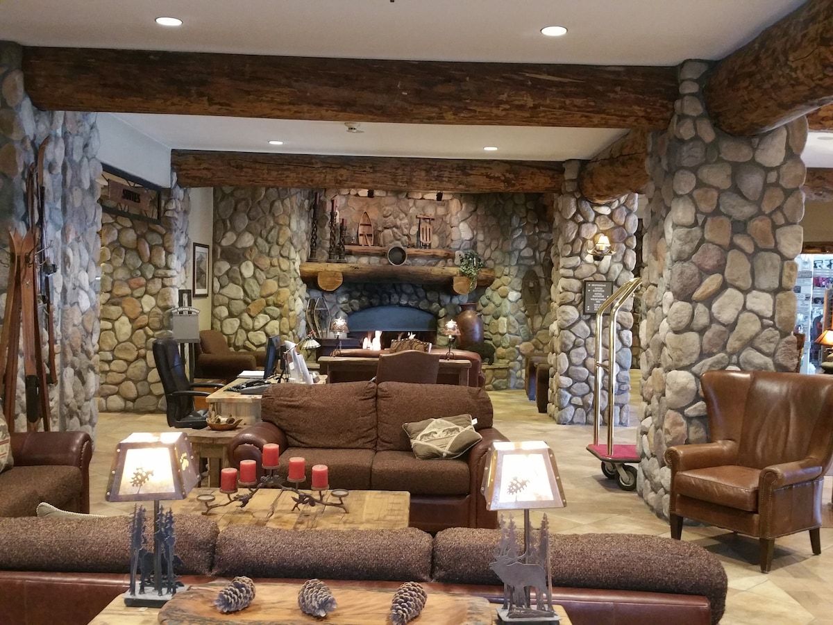 A cozy living room with a stone fireplace, leather furniture, and a stone wall.