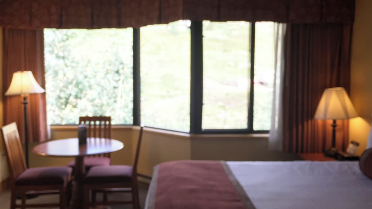 A hotel room with a bed, a table, two chairs, and a window with curtains.